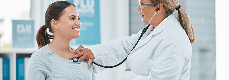 A medical professional listens to a woman's chest with a stethoscope